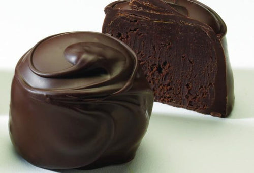 An image of a chocolate truffle, with one whole and one cut in half to show the cherry center, on a white background.