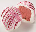 A photo of two cherry cheesecake truffles, one whole and one cut in half to show the filling, with white chocolate coating and pink drizzle.