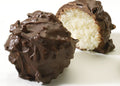 Two chocolate covered coconut truffles on a white surface, one whole and one cut in half to show the creamy coconut center.