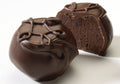 Two pieces of dark chocolate truffles with a raspberry purée filling, coated with a glazing chocolate on top.