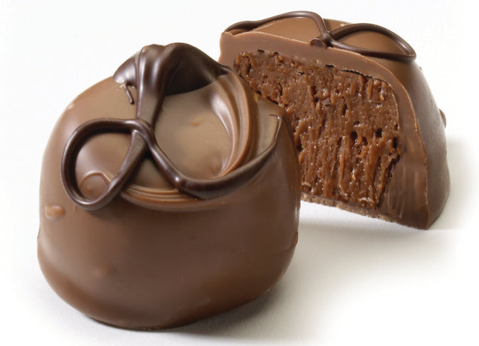 An image showing a whole and a sliced chocolate truffle, revealing the whipped cream center, set on a white background.