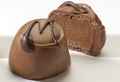 An image showing a chocolate mousse truffle cut in half, with a creamy brown center visible, surrounded by a dark chocolate shell.