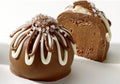 A chocolate truffle with a white and dark chocolate coating, sprinkled with sugar crystals, presented on a white plate.