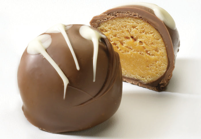 Two chocolate covered truffles with a creamy center, one intact and the other cut in half to show the peanut butter filling, on a white background.