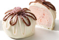 A photo of two truffles, one intact with a white chocolate coating and a sprinkle of sugar crystals on top, and the other cut in half revealing a pink and white layered truffle with a dollop of red sauce on top.
