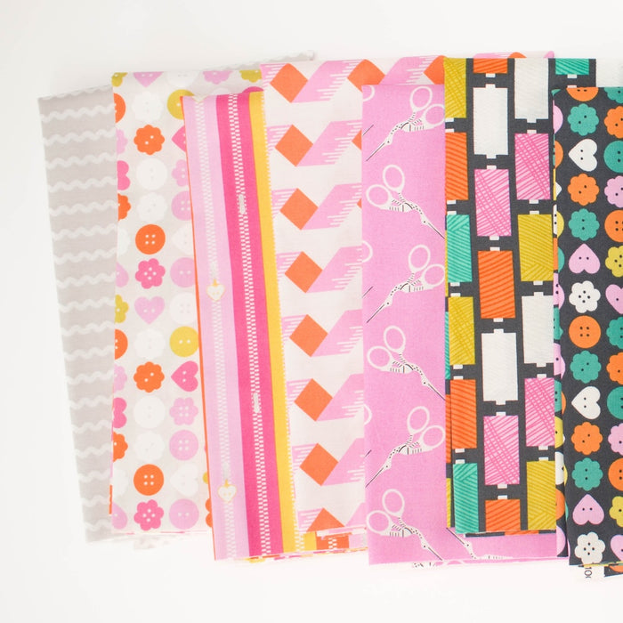 A stack of colorful patterned fabric sheets fanned out on a white background, featuring designs with buttons, zigzags, zipper stripes, scissors, and thread spools.
