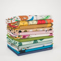 A stack of folded patterned fabric pieces in various colors and designs, including botanical leaf prints, polka dots, and floral motifs, photographed on a clean white background.