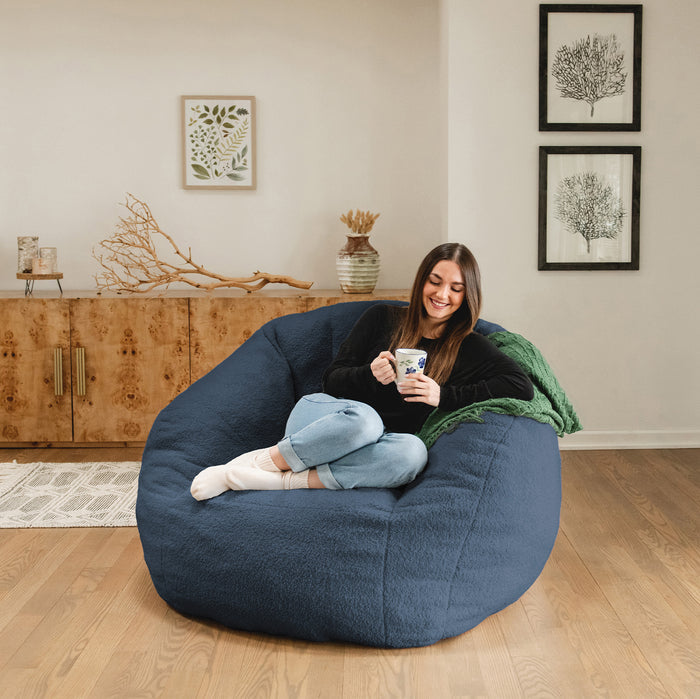 Woman sitting on a large blue bean bag chair in a living room, holding a mug. #color_slate-blue-teddy-boucle