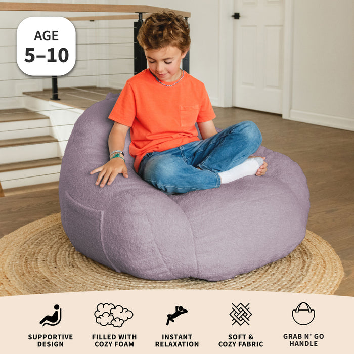 Child sitting on a purple bean bag chair in a home setting with product features displayed below. #color_lilac-teddy-boucle