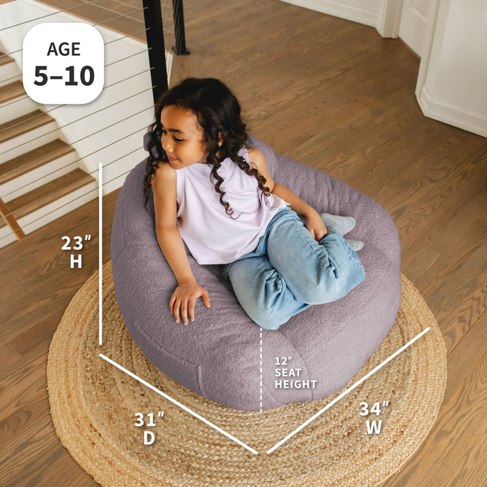 Child sitting on a bean bag chair with dimensions displayed, on a wooden floor. #color_lilac-teddy-boucle