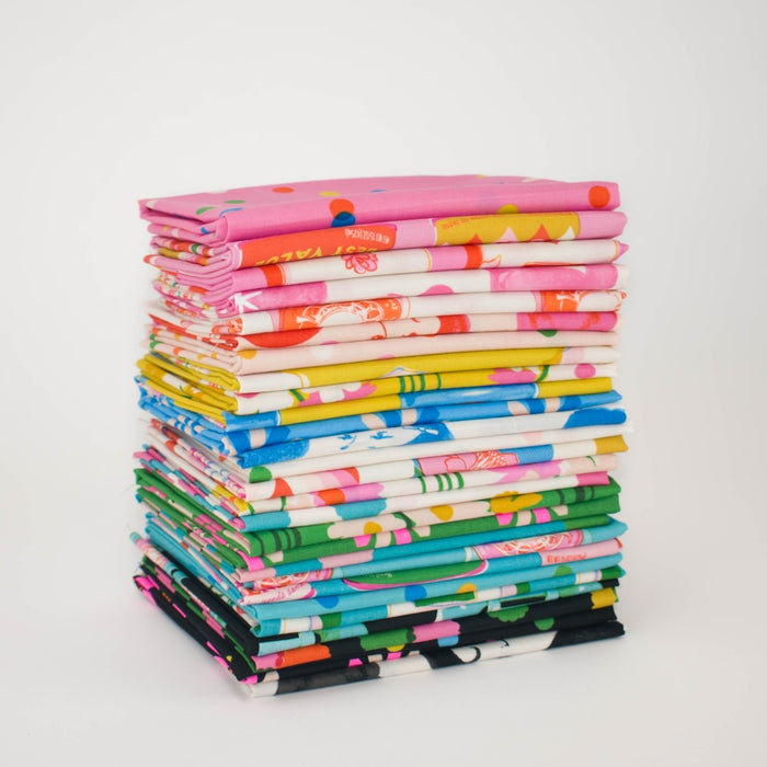 A tall stack of folded fabric pieces in assorted bright colors and patterns, including pink, yellow, blue, green, cream, and black, photographed on a clean white background.