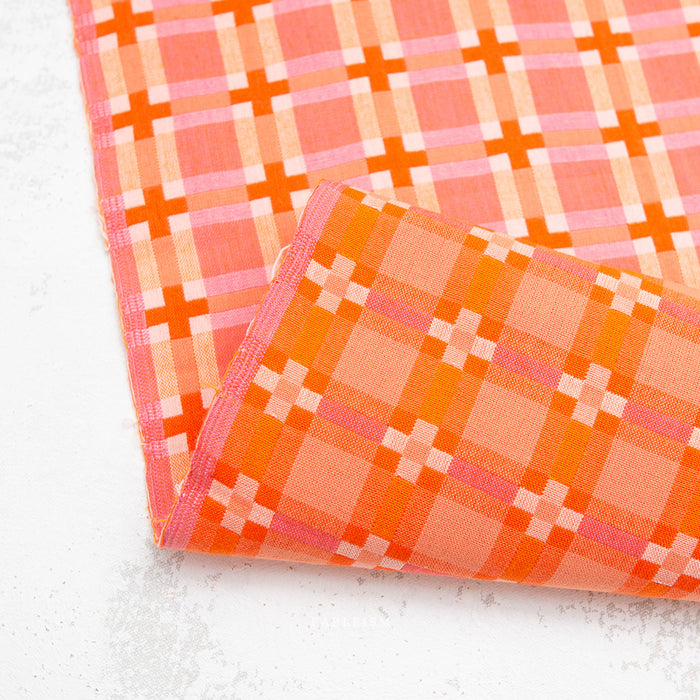 Reversible angle of plaid fabric with orange and pink pattern on a textured surface
