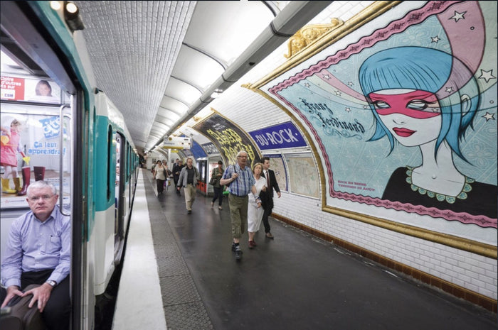 People walking in a subway station with a colorful muralby Tara McPherson on the wall.