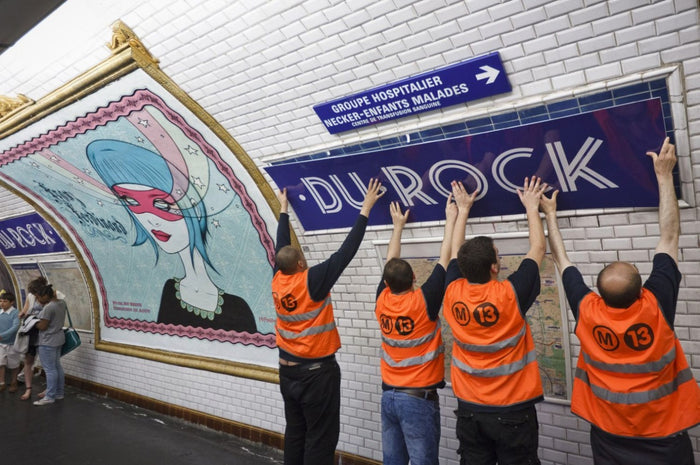 People in orange vests replacing th Duroc Metro Sign with a Du Rock sign