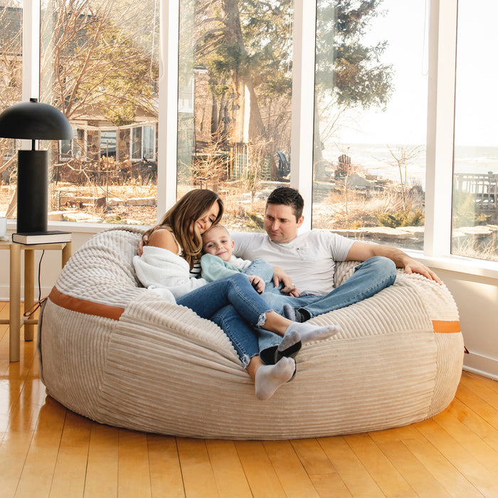 Family sitting on a bean bag in a modern living room with large windows. #color_vanilla-latte-corded-plush