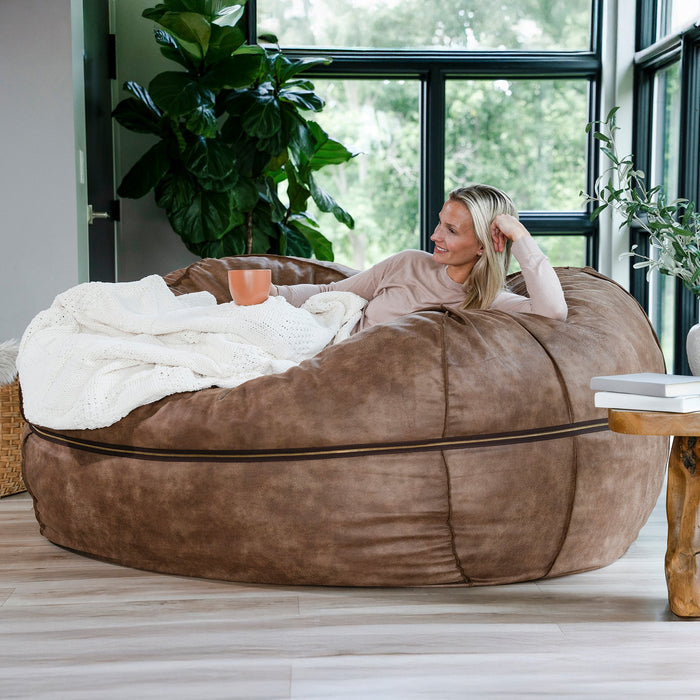 Woman relaxing on a oversized brown bean bag chair in a bright room with plants. #color_coffee-soft-vegan-leather