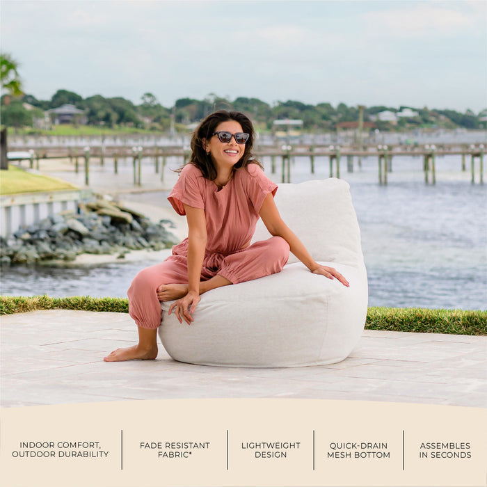 Woman sitting on a white outdoor chair by a waterfront with text about chair features. #color_sunlit-ivory-outdoor-performance-linen