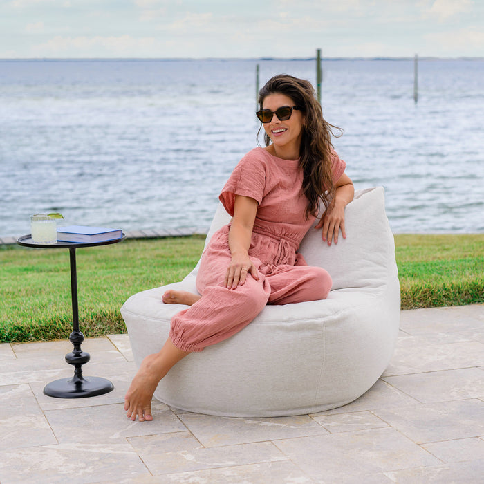 Woman relaxing on the Luft Bean Bag Chair Patio Furniture #color_sunlit-ivory-outdoor-performance-linen