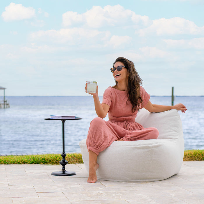 Woman with drink chatting on the Luft Chair #color_sunlit-ivory-outdoor-performance-linen