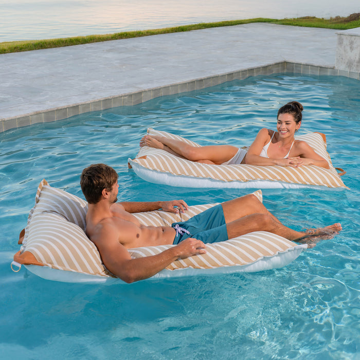 Two people relaxing on striped bean bags in a pool. #color_sand-stripe-sunbrella-fabric