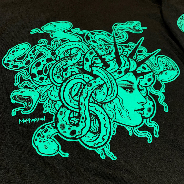 Close-up of a black garment featuring a large neon green graphic of Medusa with snakes and the signature 'McPherson' on the fabric.