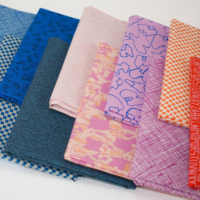 A fan-like arrangement of folded patterned fabric pieces in multiple colors and prints, including blue, pink, purple, orange, and red, photographed on a white background.