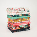 A stack of folded fabric pieces with various holiday-themed patterns, including cocktails, snowflakes, stars, candy, and ornaments, set against a plain white background.