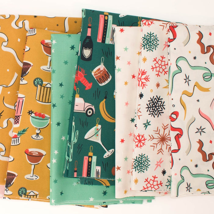 A stack of seven patterned fabrics in different colors and designs, including yellow cocktail prints, star prints, cream snowflakes, and multicolor ornaments, arranged on a white background.