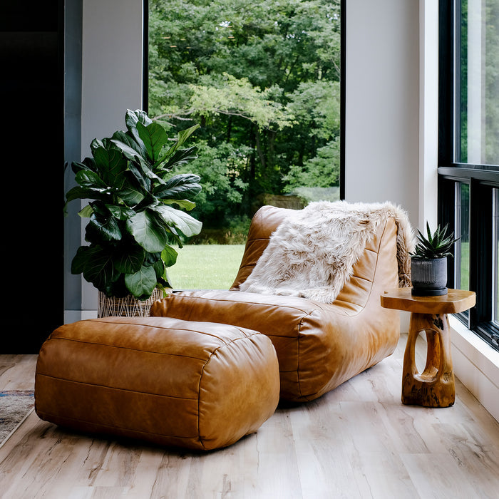 Brown leather lounge chair and ottoman with a wooden side table in a room with large windows. #color_copper-harbor-premium-vegan-leather