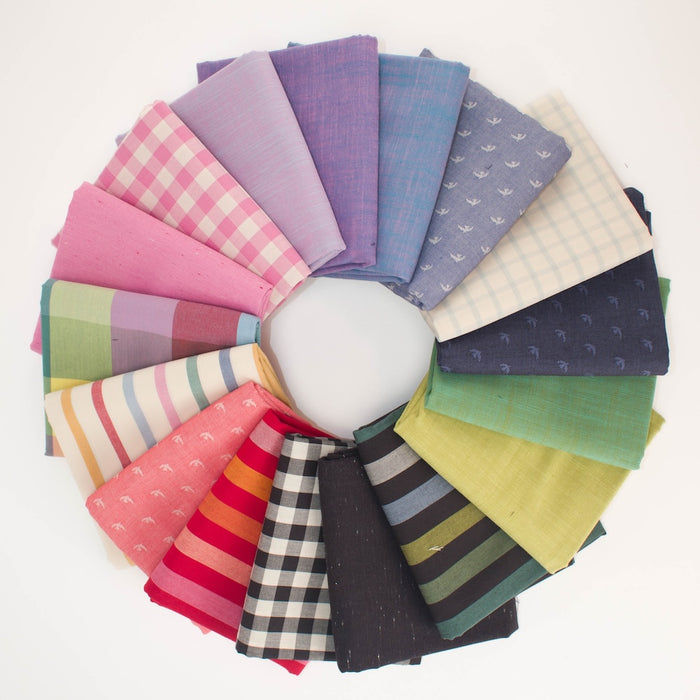 A circular arrangement of folded fabric pieces in multiple colors and patterns, including pink gingham, lavender, blue, cream plaid, green, yellow, orange stripes, black-and-white gingham, and striped fabrics, displayed on a white background.