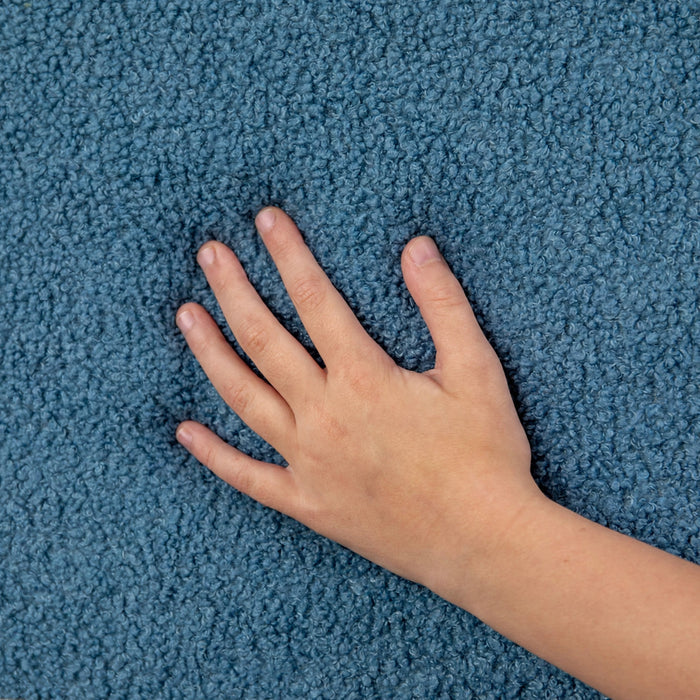 A close-up of a textured blue carpet with a child's hand and arm resting on it to show the pile height and texture. #style_blue-dinosaur