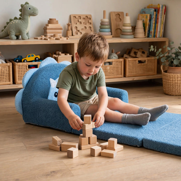 A young boy sits on a blue plush floor chair in a bright children's room, stacking wooden blocks in front of him. Shelves in the background hold toys, books, and storage baskets. #style_blue-dinosaur