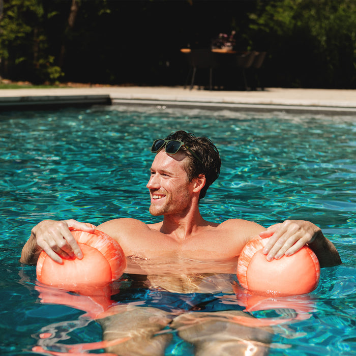 Man floating in a pool with two pink bouys #color_peach-glow
