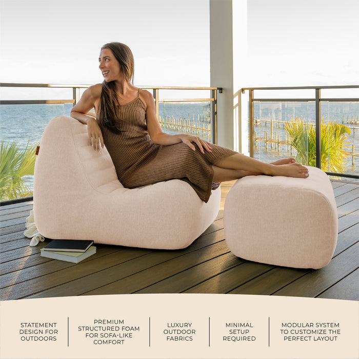 Woman sitting on a beige chair on a deck with ocean view #color_sunlit-cream-outdoor-performance-linen