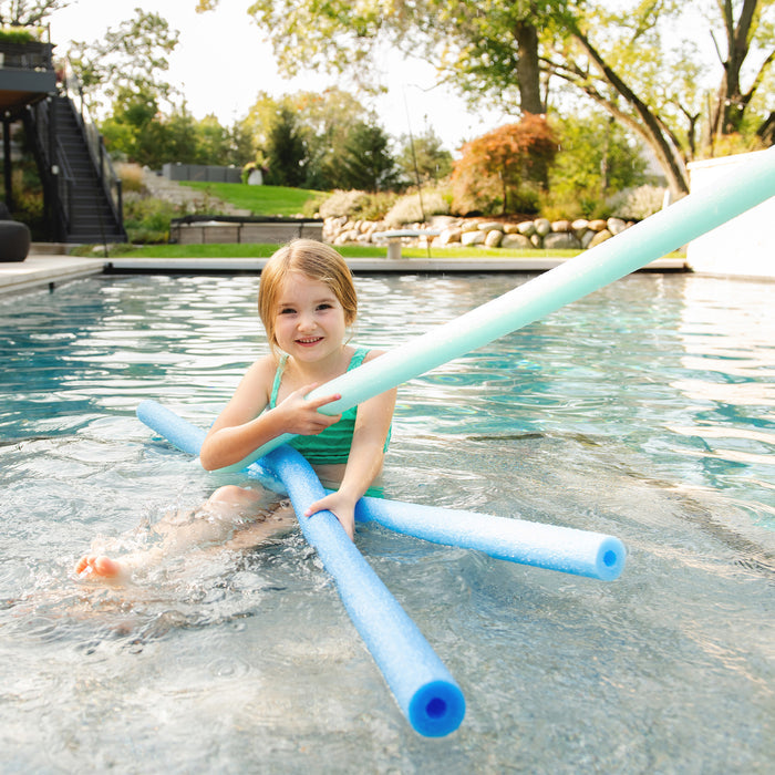 A young girl sitting in a swimming pool holding several blue and mint green pool noodles. #color_blues