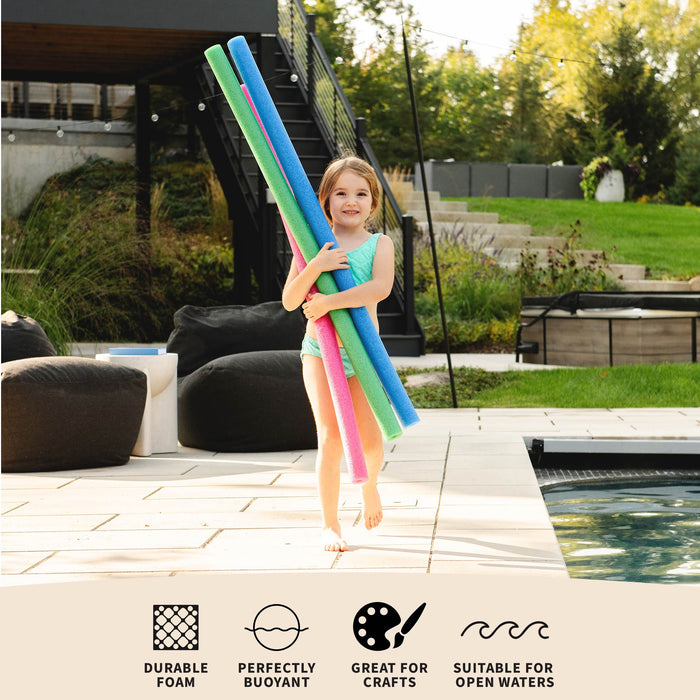 A young girl stands on a pool deck holding three long pool noodles in blue, green, and pink. The background shows a backyard patio, lounge chairs, a staircase, and a swimming pool. #color_blue-green-pink