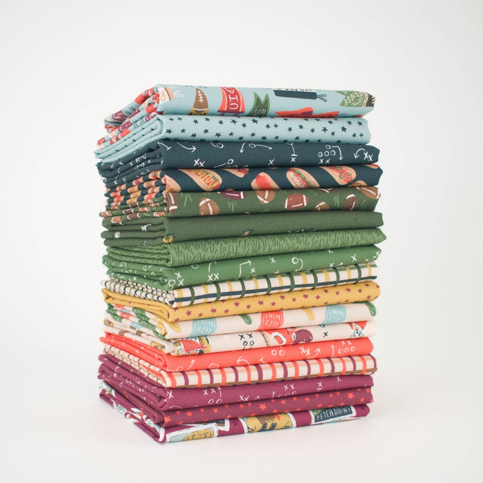 A tall stack of folded fabrics in assorted colors and dog football themed patterns, including greens, blues, reds, oranges, yellows, and whites, photographed on a clean white background.