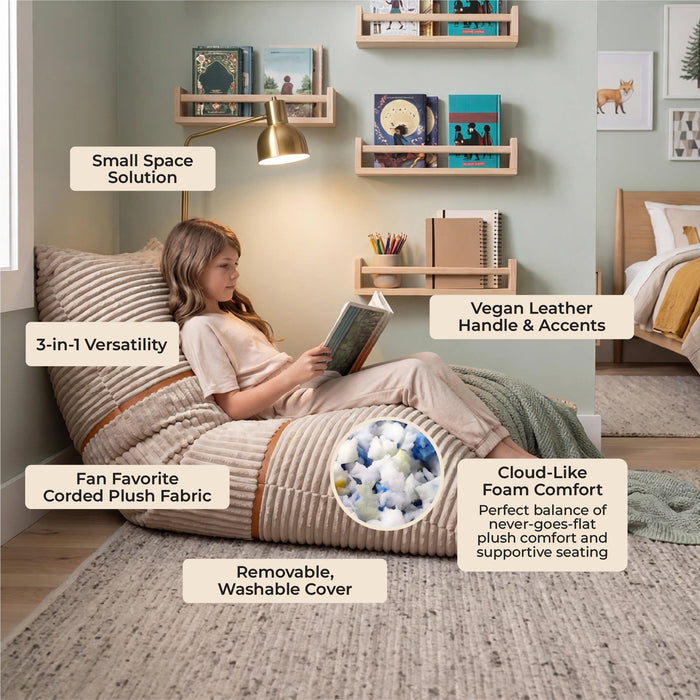 A child sits on a large upholstered bean bag chair in a styled bedroom. The bean bag has a beige corded fabric cover with a striped pattern and a matching handle. #color_vanilla-latte-corded-plush