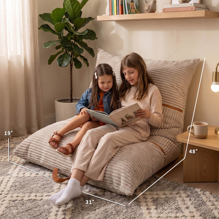Two people sitting on a large striped beige lounge floor cushion in a cozy room, with white dimension lines showing the cushion's measurements: 19 inches wide, 31 inches deep, and 48 inches tall. #color_vanilla-latte-corded-plush