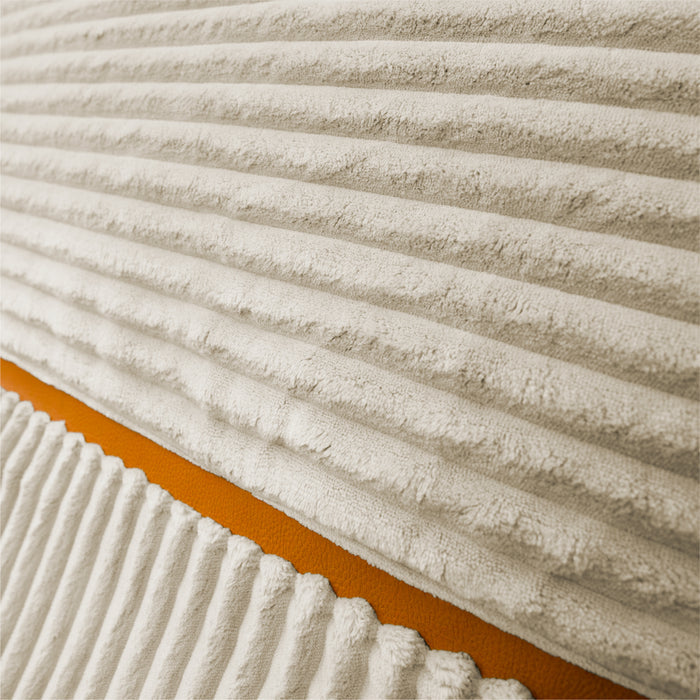 Close-up of a ribbed corduroy fabric in warm off-white, with a diagonal orange accent stripe visible along the lower left. #color_vanilla-latte-corded-plush