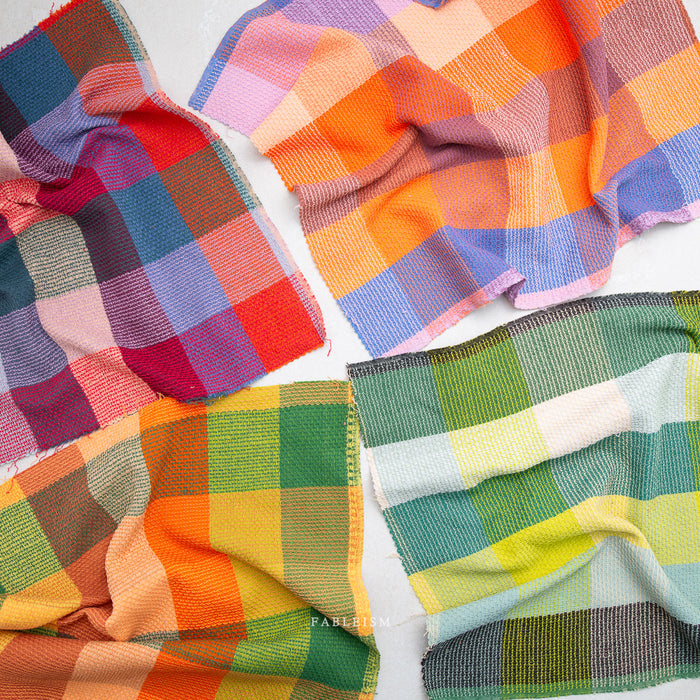 Four folded plaid fabric cloths in different color combinations, arranged on a white background.