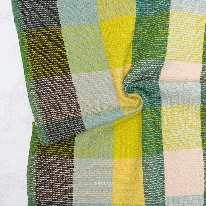 Close-up of a plaid fabric with green, yellow, and brown colors on a white background.