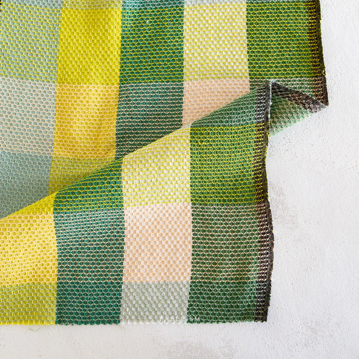 Checkered fabric with green, yellow, and beige squares on a white background